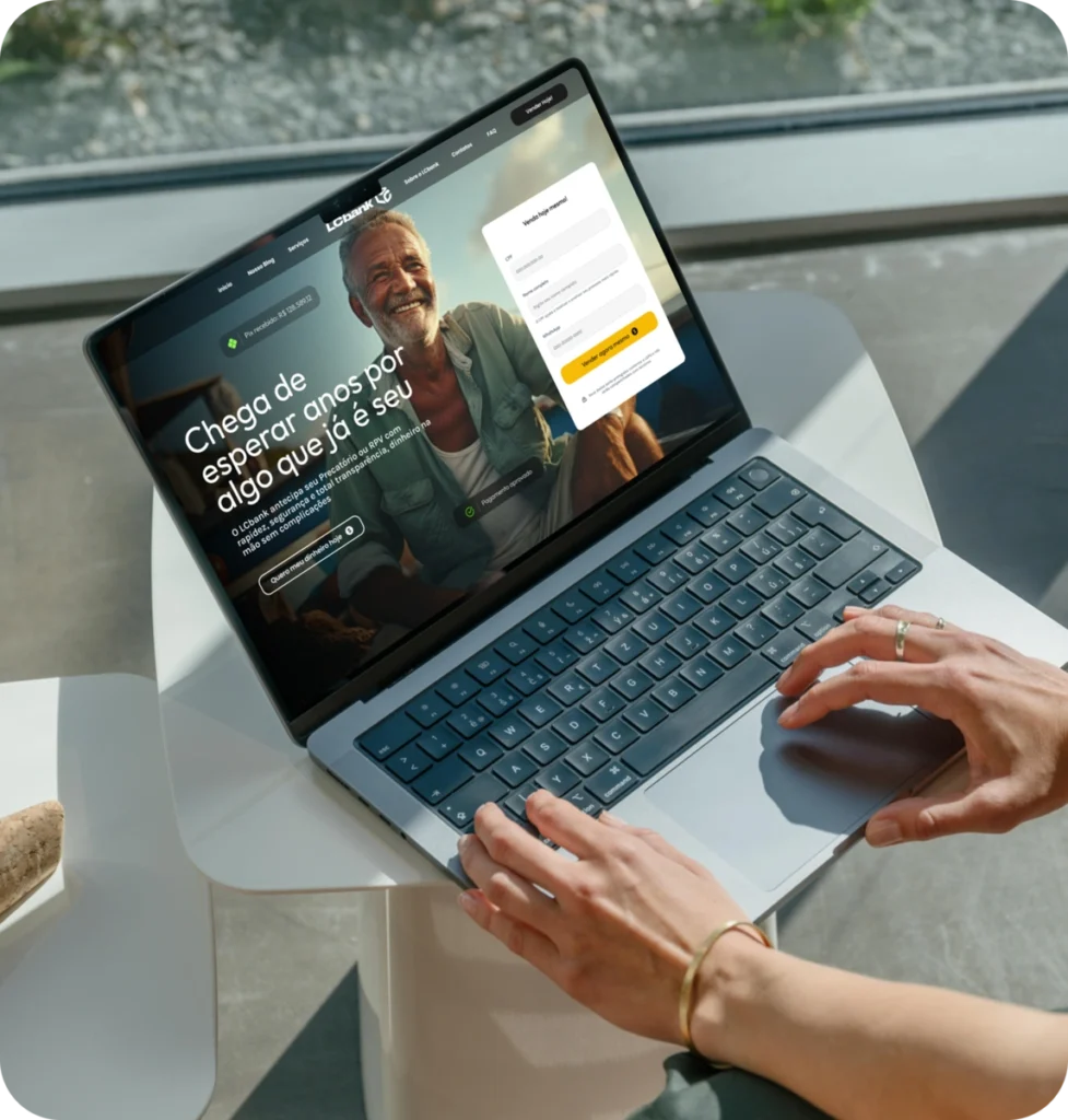 Mãos digitando em um laptop com a tela mostrando LCbank e um homem sorridente